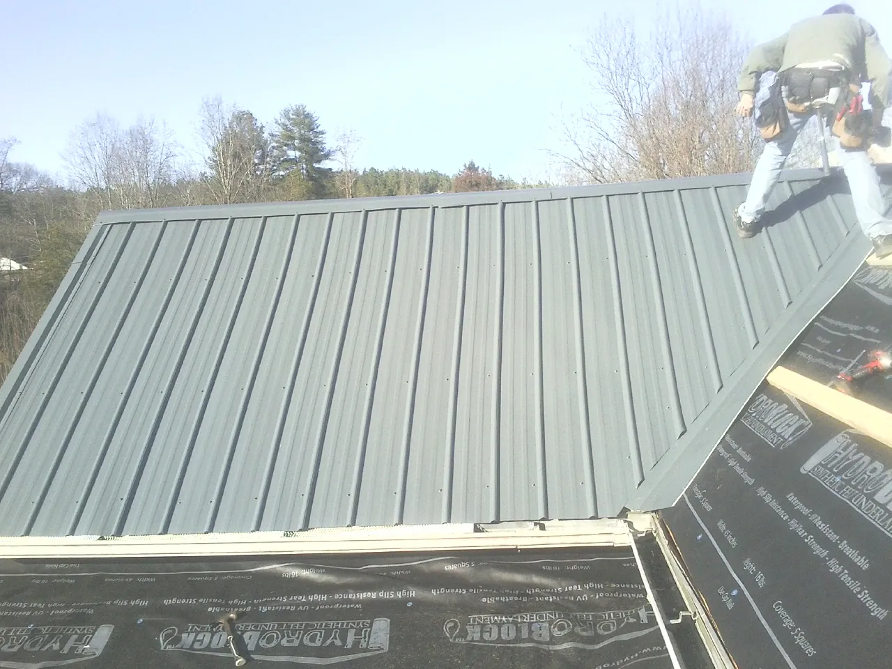 Crew installing dark green standing seam panels over synthetic underlayment in Battle Lake