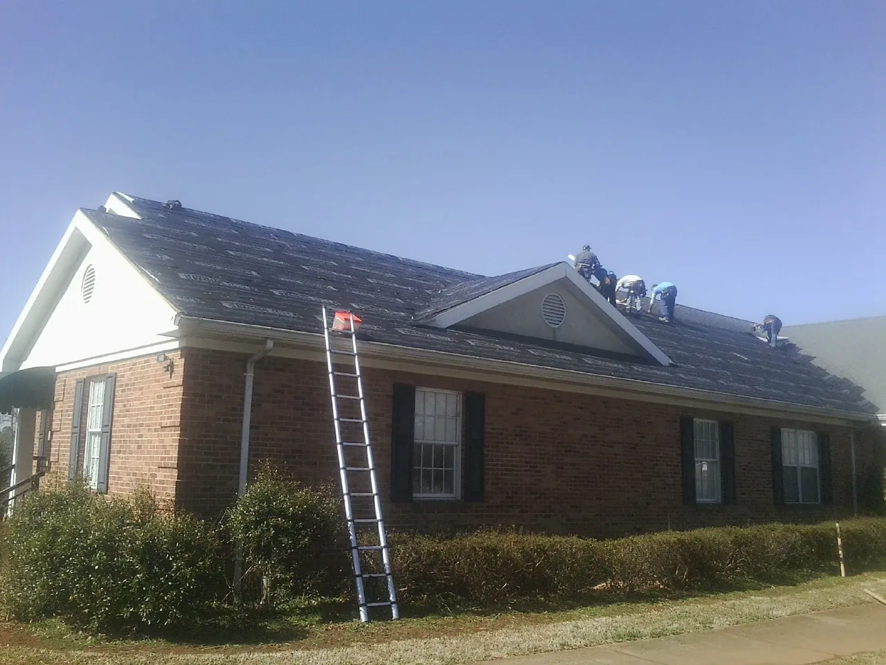 Crew tearing shingles off a brick ranch roof with a ladder set — Metal Roof Repair work by our crew in Battle Lake