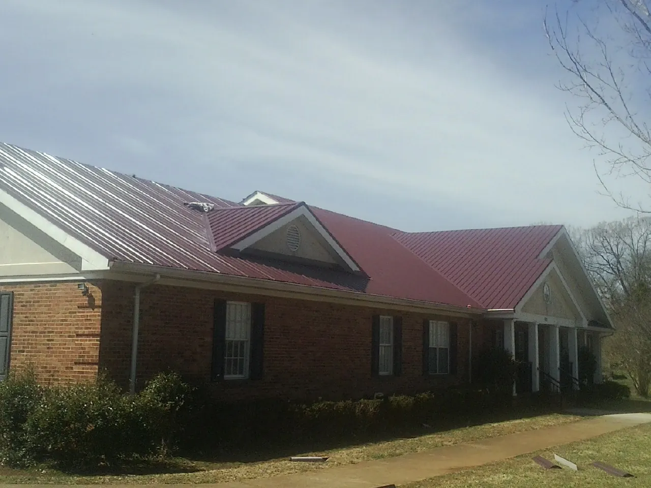 Red metal roof with gabled entries on a long brick building, from a Hail Damage Roof Repair job in Battle Lake