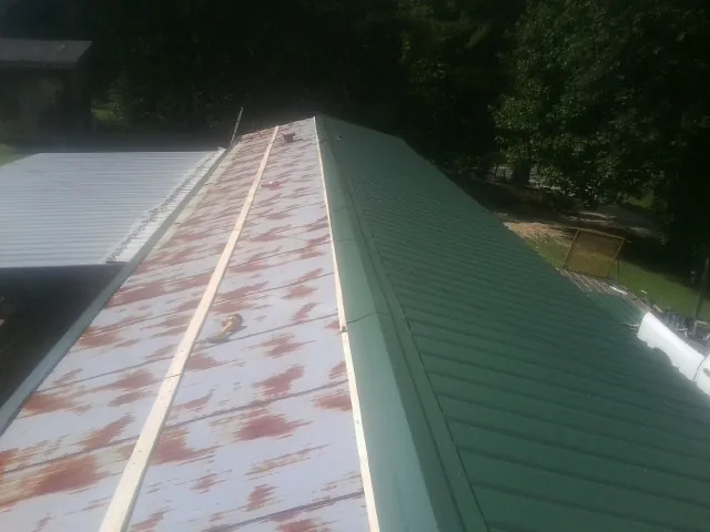 Old rusted panels beside newly installed green metal roofing — Wind Damage Roof Repair by Roofing Brothers in Battle Lake