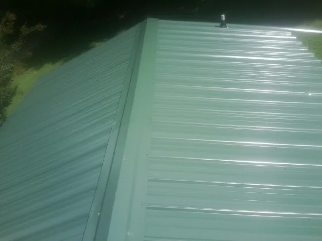 New green metal panels meeting at the ridge of a roof — Flat Roof Repair work by our crew in Battle Lake
