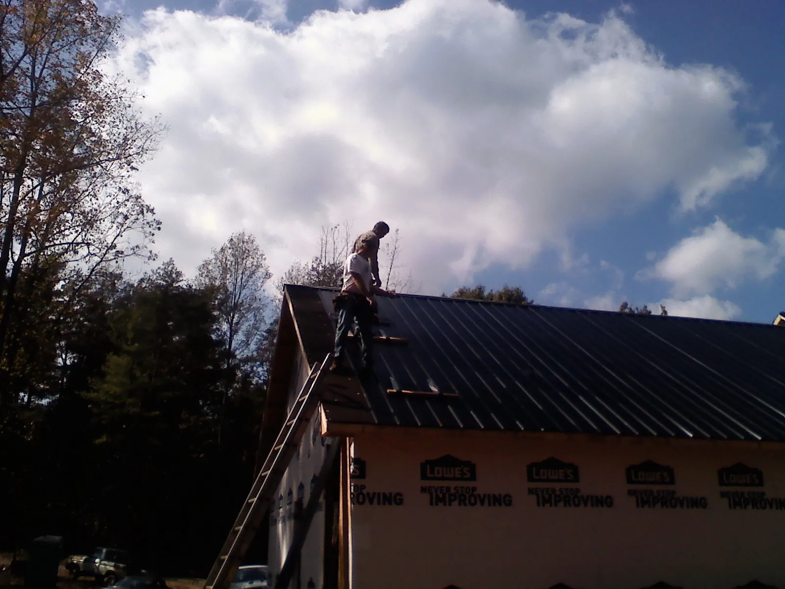 Roofer fastening dark metal panels high against a cloudy sky, from a Roof Inspection job in Battle Lake