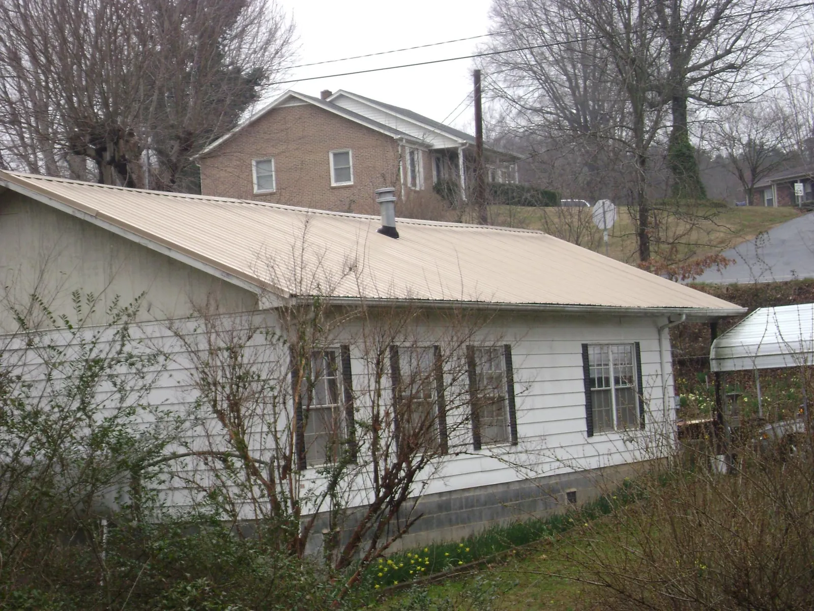 Tan metal roof on a white sided house set into a hillside — Commercial Roofing by Roofing Brothers in Battle Lake