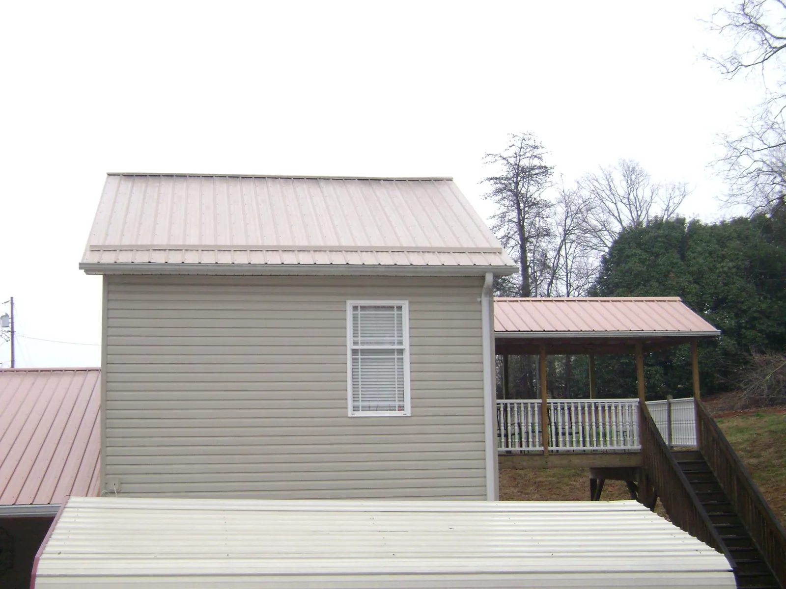 Tan metal roofs on a two story addition and attached porch, from a Roof Replacement job in Battle Lake